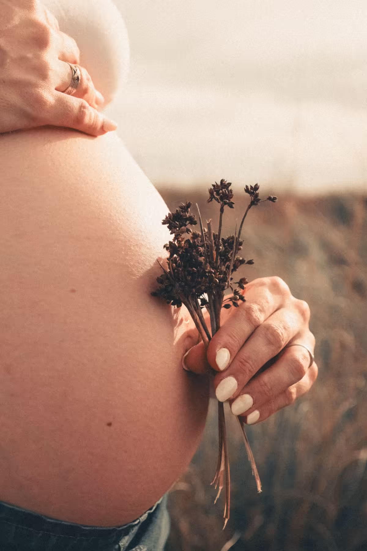 Mulher grávida segura pequenas flores junto à barriga