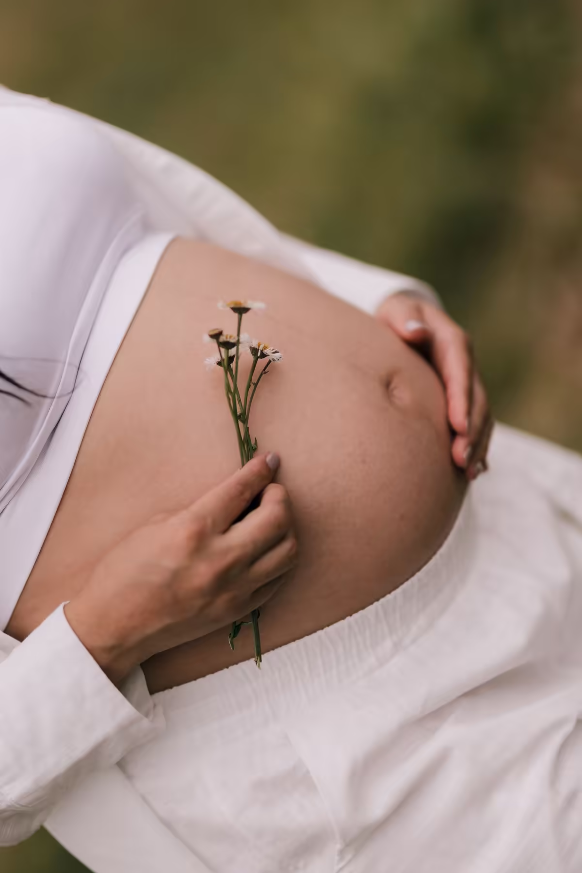 Mulher grávida vestida de branco segura pequenas flores sobre a barriga